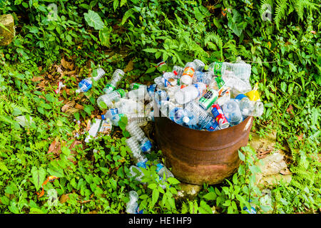 Müll wie leere Plastikflaschen wird im rostigen Fass gefüllt, einige Flaschen auf dem Boden gesammelt. Stockfoto