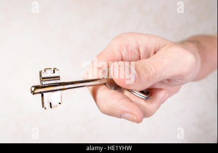 Die Hand eines Mannes hält einen Schlüssel, öffnen oder Schließen einer Tür, auf hellem Hintergrund Stockfoto