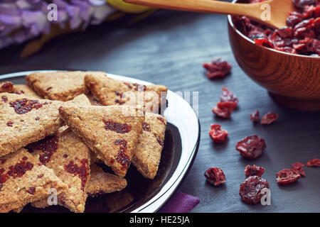 Vollkorn-Kekse mit getrockneten Cranberries auf schwarzem Hintergrund aus Holz Stockfoto