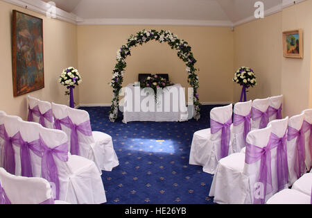 Ein Zimmer für eine Trauung mit einem Bogen aus Blumen und weiße Stühle mit rosa Schleifen bereit gelegt Stockfoto