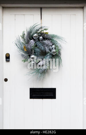 Dekorativer Weihnachtskranz an einem weißen Eingangstür hängen. Stockfoto