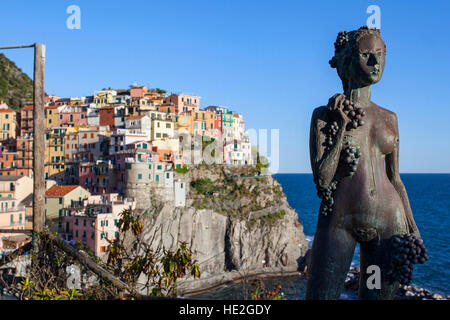 Eine Hommage an den Wein: die Statue einer Frau mit Trauben und die Stadt von Manarola im Hintergrund. Cinque Terre, Ligurien, Italien. Stockfoto