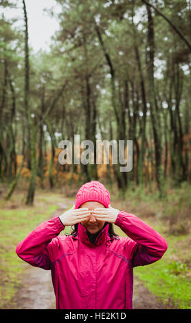 Frau mit rosa Wollmütze in den Wald für ihre Augen Stockfoto