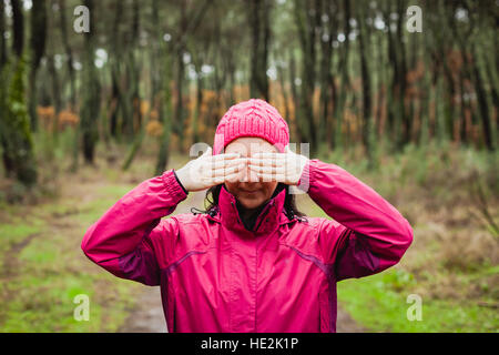 Frau mit rosa Wollmütze in den Wald für ihre Augen Stockfoto