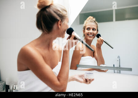 Schöne junge Frau mit Pinsel auftragen von Make-up im Badezimmer. Weibliche Blick in den Spiegel und setzen auf Make-up. Stockfoto