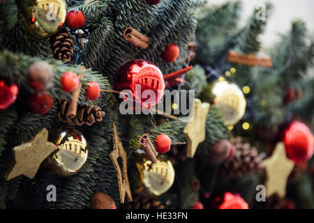 Weihnachtsschmuck mit Tannengrün, roten und goldenen Kugeln und Sternen auf. Reflexionen von Straße, Gebäude und Menschen in den Dreh raus Stockfoto