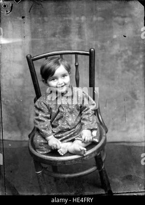Ein historisches Foto eines Kindes, das auf einem Stuhl sitzt, aufgenommen von Costica Acsinte in Rumänien mit einem Folienfilm. Stockfoto