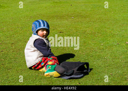 Eine kleine, lokale Junge in warme, farbige Tücher sitzt auf einer grünen Wiese Stockfoto