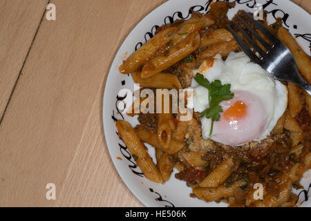 Penne all' Arrabbiata mit einem frisch pochierten Ei garniert. Stockfoto