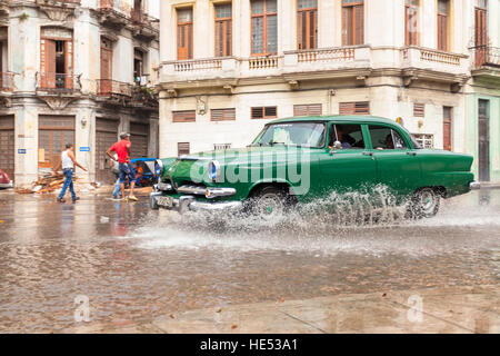 Ein grüner Oldtimer durchläuft eine Pfütze nach einem Starkregen in Alt-Havanna, Kuba. Stockfoto