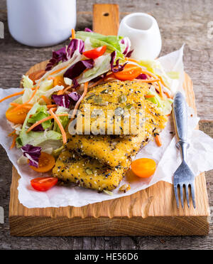 Beschichtete Fischfilet mit frischem Salat serviert auf Holzbrett Stockfoto