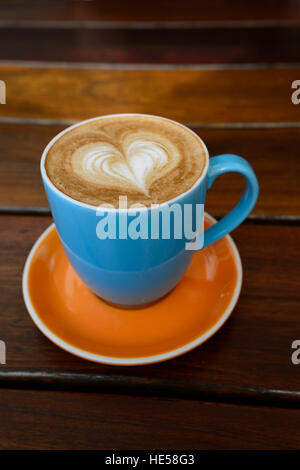 Eine Tasse Latte mit der Form eines Herzens auf eine Untertasse auf einem Tisch platziert Stockfoto