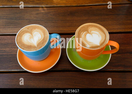 Zwei bunte Tassen Café Latte mit der Form eines Herzens auf eine Untertasse auf einem Tisch platziert Stockfoto