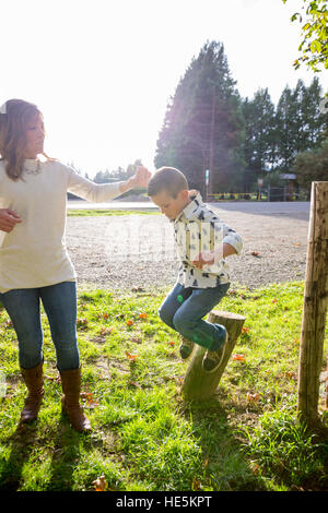 Junge, springen von einem hölzernen Pfosten während an der Hand seiner Mutter in einem Park. Stockfoto