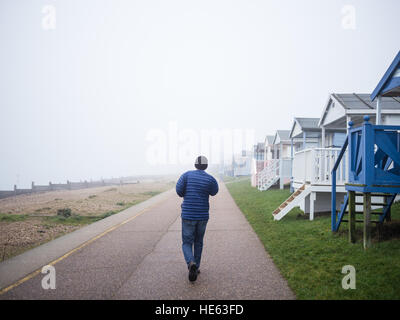 Whitstable, Großbritannien. 18. Dezember 2016. Das Wetter in Kent. Eine Mann geht auf Tankerton Promenade vorbei an hölzernen Strandhütten entlang der Strandpromenade auf einem sehr nebligen, neblig, nachmittags in Kent. Bildnachweis: CBCK-Christine/Alamy Live-Nachrichten Stockfoto