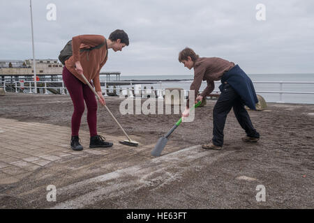 Aberystwyth Wales UK, Sonntag, 18. Dezember 2016 Aberystwyth University Studenten ELEANOR CLIFTON (22, Bürsten) und XANDER König (20, mit Schaufel), beide ursprünglich aus Wiltshire, habe alle von diesem Sonntagnachmittag Bürsten und Schaufeln Sand abseits die Promenade in Aberystwyth nach der stürmischen See Anfang dieser Woche. Sie haben sich auf eigene Faust, ohne Zutun der Gemeindebehörde Eleanors Partner zu ermöglichen, die ein Rollstuhl-Benutzer ist, und viele andere Leute eingeschränkten Mobilität, in den Genuss die Strandpromenade Credit: Keith Morris/Alamy Live-Nachrichten Stockfoto