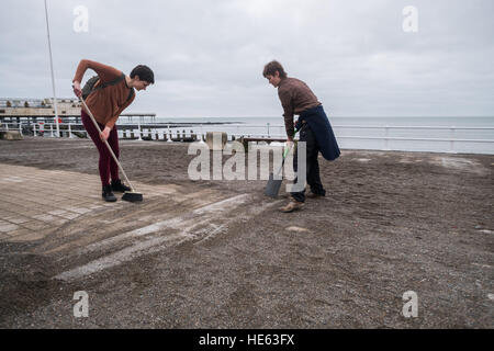 Aberystwyth Wales UK, Sonntag, 18. Dezember 2016 Aberystwyth University Studenten ELEANOR CLIFTON (22, Bürsten) und XANDER König (20, mit Schaufel), beide ursprünglich aus Wiltshire, habe alle von diesem Sonntagnachmittag Bürsten und Schaufeln Sand abseits die Promenade in Aberystwyth nach der stürmischen See Anfang dieser Woche. Sie haben sich auf eigene Faust, ohne Zutun der Gemeindebehörde Eleanors Partner zu ermöglichen, die ein Rollstuhl-Benutzer ist, und viele andere Leute eingeschränkten Mobilität, in den Genuss die Strandpromenade Credit: Keith Morris/Alamy Live-Nachrichten Stockfoto