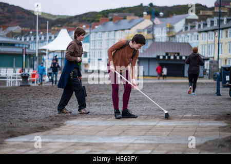 Aberystwyth Wales UK, Sonntag, 18. Dezember 2016 Aberystwyth University Studenten ELEANOR CLIFTON (22, Bürsten) und XANDER König (20, mit Schaufel), beide ursprünglich aus Wiltshire, habe alle von diesem Sonntagnachmittag Bürsten und Schaufeln Sand abseits die Promenade in Aberystwyth nach der stürmischen See Anfang dieser Woche. Sie haben sich auf eigene Faust, ohne Zutun der Gemeindebehörde Eleanors Partner zu ermöglichen, die ein Rollstuhl-Benutzer ist, und viele andere Leute eingeschränkten Mobilität, in den Genuss die Strandpromenade Credit: Keith Morris/Alamy Live-Nachrichten Stockfoto