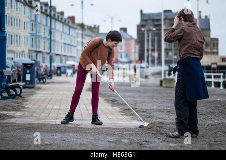 Aberystwyth Wales UK, Sonntag, 18. Dezember 2016 Aberystwyth University Studenten ELEANOR CLIFTON (22, Bürsten) und XANDER König (20, mit Schaufel), beide ursprünglich aus Wiltshire, habe alle von diesem Sonntagnachmittag Bürsten und Schaufeln Sand abseits die Promenade in Aberystwyth nach der stürmischen See Anfang dieser Woche. Sie haben sich auf eigene Faust, ohne Zutun der Gemeindebehörde Eleanors Partner zu ermöglichen, die ein Rollstuhl-Benutzer ist, und viele andere Leute eingeschränkten Mobilität, in den Genuss die Strandpromenade Credit: Keith Morris/Alamy Live-Nachrichten Stockfoto