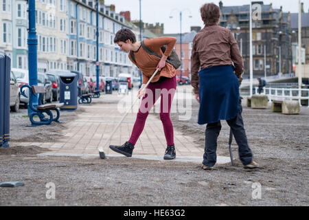 Aberystwyth Wales UK, Sonntag, 18. Dezember 2016 Aberystwyth University Studenten ELEANOR CLIFTON (22, Bürsten) und XANDER König (20, mit Schaufel), beide ursprünglich aus Wiltshire, habe alle von diesem Sonntagnachmittag Bürsten und Schaufeln Sand abseits die Promenade in Aberystwyth nach der stürmischen See Anfang dieser Woche. Sie haben sich auf eigene Faust, ohne Zutun der Gemeindebehörde Eleanors Partner zu ermöglichen, die ein Rollstuhl-Benutzer ist, und viele andere Leute eingeschränkten Mobilität, in den Genuss die Strandpromenade Credit: Keith Morris/Alamy Live-Nachrichten Stockfoto