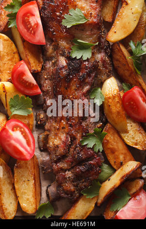 Gegrilltes Schweinefleisch Rippen, Kartoffeln und Tomaten Makro. vertikale Ansicht von oben Stockfoto