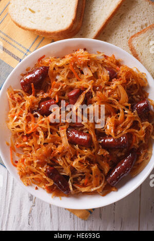 Geschmortes Sauerkraut mit Würstchen Nahaufnahme in weißen Teller. vertikale Ansicht von oben Stockfoto