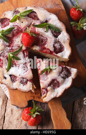 Haus in Scheiben geschnitten Erdbeertorte mit Minze auf ein Schneidebrett. Vertikale Ansicht von oben. Rustikaler Stil Stockfoto