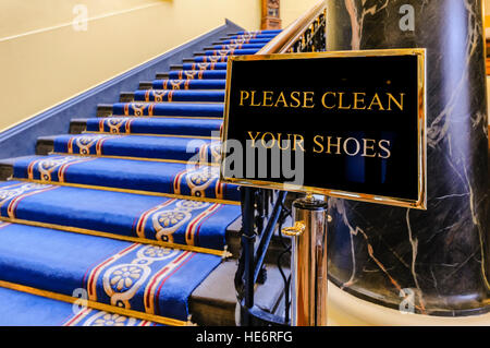 Unterschreiben Sie sagen "Bitte reinigen Sie Ihre Schuhe" am unteren Ende der Treppe in einem großen, reich verzierten Gebäude. Stockfoto