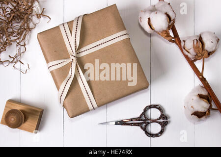 Geschenkbox mit Leerzeichen, Mockup Draufsicht. Fertige Gegenstände festgelegt. Blume aus Holz Hintergrund, Stempel, Scheren und Baumwolle. Stockfoto