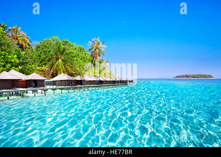 Overwater Bungalows auf tropischen Insel mit Sandstrand, Palmen und türkisfarbenem klarem Wasser Stockfoto