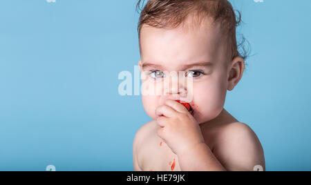 Baby kaute saure Erdbeere und Squint Gesicht ziehen Stockfoto