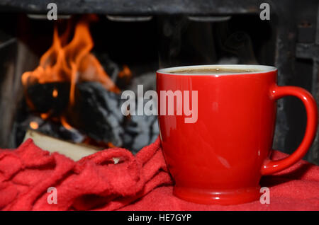 Rote Tasse auf einer roten weichen Decke mit Feuer Form einen Kamin im Hintergrund Stockfoto