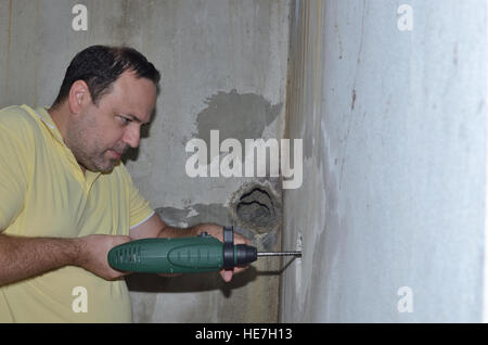 Mann hält elektrische Bohrmaschine und Bohrung in einer Betonwand Stockfoto