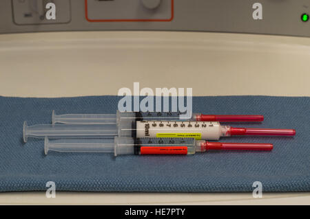 Drei Spritzen mit roten angeschnittene Ärmel Nadeln enthalten allgemeine Anästhesie Medikamente mit Anästhesiegerät im Hintergrund gekennzeichnet. Stockfoto