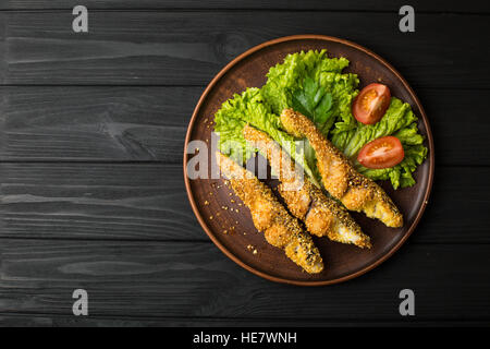 Gebratener Fisch mit Salat und Tomaten auf einem schwarzen Holztisch Stockfoto