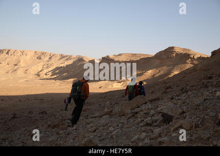 Senioren-Wanderer Fuß in Makhtesh Ramon bei Sonnenaufgang, sie sind im Schatten die Wand auf der linken Seite wird durch die aufgehende Sonne beleuchtet. Stockfoto