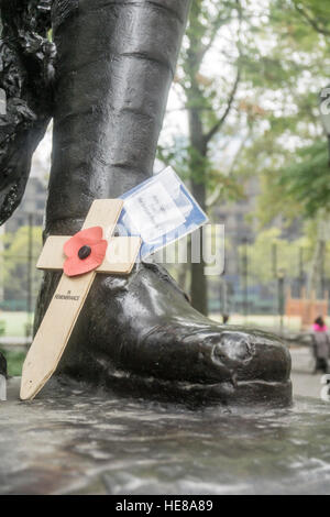 kleine hölzernes Kreuz verziert mit roter Mohn & Worte in Erinnerung lehnt sich gegen Bronze Boot Doughboy Statue im Herbst park Stockfoto