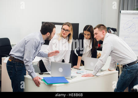 Willkommen Sie an Bord. Vier am Tisch während zwei von ihnen Geschäftsleute Händeschütteln und lächelnd Stockfoto