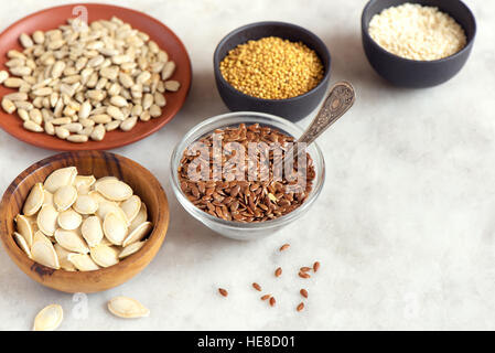 Ölsaaten (Flachs, Sesam, Kürbis, Sonnenblume, Senf) in kleinen Schalen auf Stein Hintergrund - Bio-Zutaten für gesunde vegetarische vegane n sortiert Stockfoto