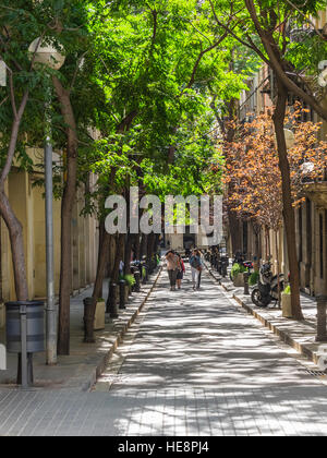Erwachsene gehen gemeinsam entlang einer schmalen Bäumen gesäumten Straße in Barcelona, Spanien. Stockfoto
