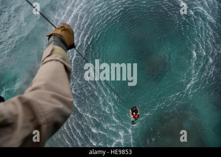 US Air Force Tech Sgt. Tyson Reams 33rd Rescue Squadron, Flugingenieur, eine Rettung Hebemaschine Kabel als Staff Sgt. Staff Sgt. Nathan Vogel, 320th Special Tactics Squadron Pararescuman Lünetten, während ein Wasser-Rettung-Szenario aus die Küste von Torii Station, Japan, 26. Februar 2013 ins Wasser abgesenkt.  Das Szenario war ein Teil eines bilateralen Trainings zwischen US-Militärangehörige, japanische Küstenwache und Einsatzkräfte. Techn. Sgt Jocelyn L. Rich-Pendracki) Stockfoto