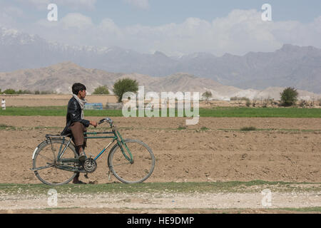 Ein afghanischer Junge hält auf seinem Fahrrad in Khanjar Khel, Parwan Provinz, Afghanistan, um als US Armee Explosive Ordnance Disposal sehen Techniker sichern die Website von einem abgestürzten f-16 Fighting Falcon von Bagram Airfield, Afghanistan. Die f-16 stürzte nach dem Start und der Pilot sicher ausgeworfen; Seitdem die Basis abgeschlossen, Bereinigen von der Absturzstelle. Die Ursache des Unfalls wird untersucht. Techn. Sgt. Robert Cloys) Stockfoto