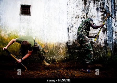 Ein US-Marine hilft eine lokale liberianischen einem Graben offen dazu ein Tor am Roberts International Airport, Republik Liberia, während Betrieb United Hilfe, 14. Oktober 2014 Graben. Die Soldat innen kehren von tragenden OUA, ein US-Verteidigungsministerium Betrieb in Liberia Logistik, Schulung und technische Unterstützung für US Agency for International Development-geführten Bemühungen, Ebola-Virus-Ausbruch in Westafrika zu begrenzen. Staff Sgt Gustavo Gonzalez Stockfoto