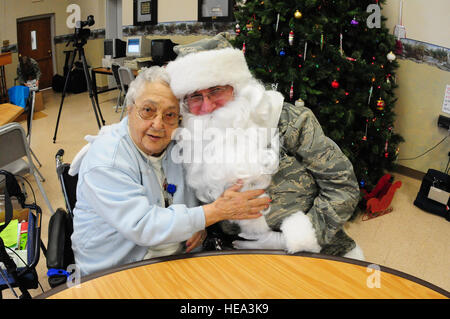 Chief Master Sgt. Paul Tangen des 119. Flügels, Dons eine speziell angefertigte Tarnung Santa zu entsprechen, wie er bekommt eine Umarmung von einem Bewohner des North Dakota Veteranen Home in Lissabon, N.D., Dezember 15, während der jährlichen North Dakota National Guard geförderte Weihnachten feiern bei den Veteranen zu Hause. North Dakota Air und Army National Guard Mitglieder Spenden persönliche Geld für Geschenke und präsentieren ihnen den Veteranen im Pflegeheim jedes Jahr während der Ferienzeit. Stockfoto