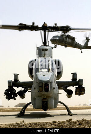 Ein uns Marine Corps (USMC) AH-1W Super Cobra-Hubschrauber mit AGM-114 Hellfire-Raketen bewaffnet und 2,75 Zoll Folding Fin Aerial Raketen (FFAR) erwartet Betankung an einer nach vorne Bereich tanken Punkt (FARP), auf Tallil Air Base, Irak während der Operation IRAQI FREEDOM. Ein US Armee (USA) UH-60 Black Hawk-Hubschrauber ist am Ansatz im Hintergrund. Stockfoto