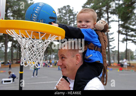 US Air Force Master Sgt. Travis Clawson, 4. Civil Engineer Squadron Systeme Feuerwehrchef, Hebezeuge, seinen Sohn zu einem Korb im Laufe des Monats den militärischen Familie Block party auf Seymour Johnson Air Force Base, North Carolina, 16. November 2013. Die Veranstaltung vorgestellten Stationen für Kinder, sich zu engagieren, wie Basketball, Mais Loch sowie eine übergroße Checker Board.  Airman 1st Class Aaron J. Jenne) Stockfoto