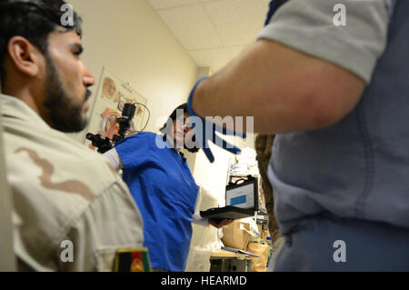 Ein medizinische Dolmetscher beobachtet, wie ein afghanischer Soldat seine übrig gebliebenen Augenmuskeln versucht um zu seinem prothetischen Okular zu bewegen, nachdem es während der Behandlung bei Craig Joint Theater Hospital in Bagram Air Field, Afghanistan 7. August 2014 in seinem leeren Sockel platziert. Der Soldat erlitt ein Trauma, als Splitter von einer Explosion ihn in seinen Augen vor vier Monaten traf. Infolgedessen, unterzog er sich Enukleation Augenchirurgie, was ist, wenn das Auge entfernt wird, aber die Augenmuskeln und orbital Restinhalt intakt bleiben.  Master Sergeant Cohen A. Young Stockfoto