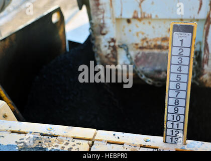 Asphalt strömt aus einem Muldenkipper in den Mund von einem Fertiger 2. Dezember 2014, in Bagram Air Field, Afghanistan. Sobald durch den Fertiger gefiltert, wird der Asphalt erhitzt und auf die Straße bei Temperaturen von über 300 Grad Fahrenheit eingeebnet. (U.S. Air Force Photo von Staff Sgt Whitney Amstutz/freigegeben) Stockfoto