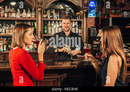 Zwei attraktive junge Frauen treffen sich in einer Kneipe für Glas Rotwein sitzen an Theke Lächeln einander Stockfoto