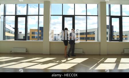 Kollegen zu Fuß entlang der Fenster im Büro und Business-Pläne zu diskutieren Stockfoto